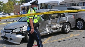 A police officer walks past one of several damaged vehicles after a car accident in a parking lot. A car crashed into the Bellagio Nails & Spa in Medford, Massachusetts, on July 28, 2020, with people inside and hitting several cars.