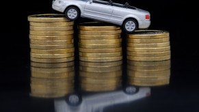 A silver Audi convertible model car rests atop three stacks of coins
