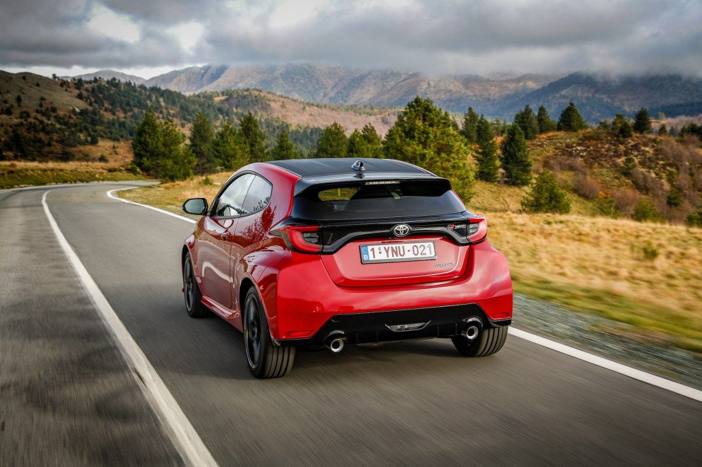 The rear 3/4 view of a red 2021 Toyota GR Yaris driving down the road
