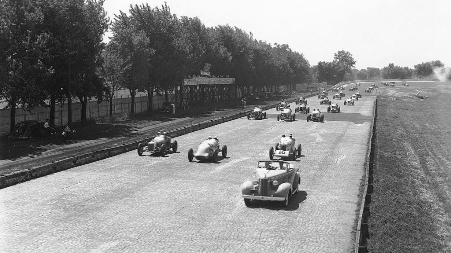 Indy cars driving on the brick racing surface of the Indianapolis Motor Speedway during the pace lap for the Indianapolis 500 in 1937
