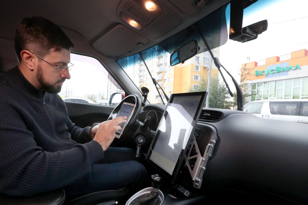 A man uses his phone as he sits in the driver's seat of a self-driving car