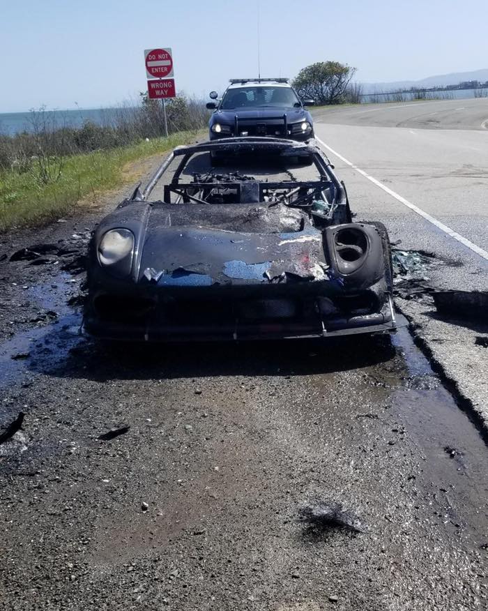 An image of a burned up Noble M400 on the side of the road.