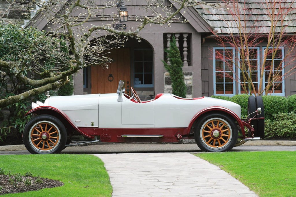 The side view of a white-and-red 1915 Crane-Simplex Model 5 46HP Boattail Tourer by an old house