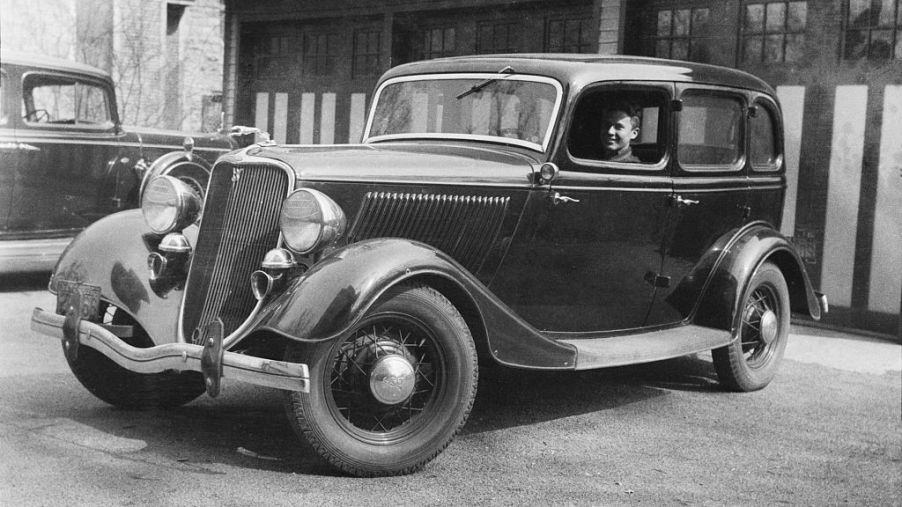 Black and white photo of a man driving a 1934 Ford Fordor, historically used as a getaway car