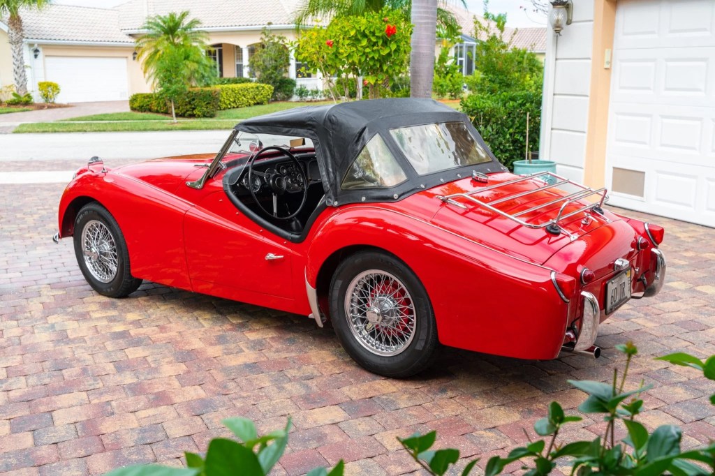 The side 3/4 view of a red TR3A-spec 1960 Triumph TR3 parked on a driveway