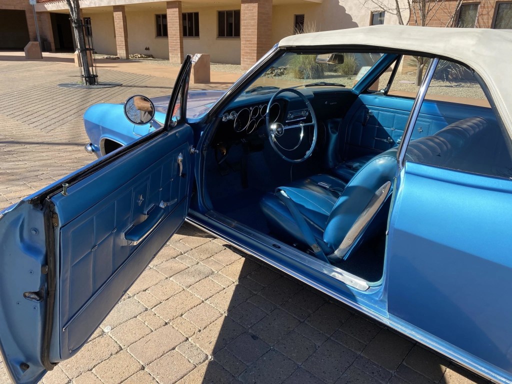 The side and blue interior of a blue 1966 Chevrolet Corvair Corsa Convertible seen from the open driver's door