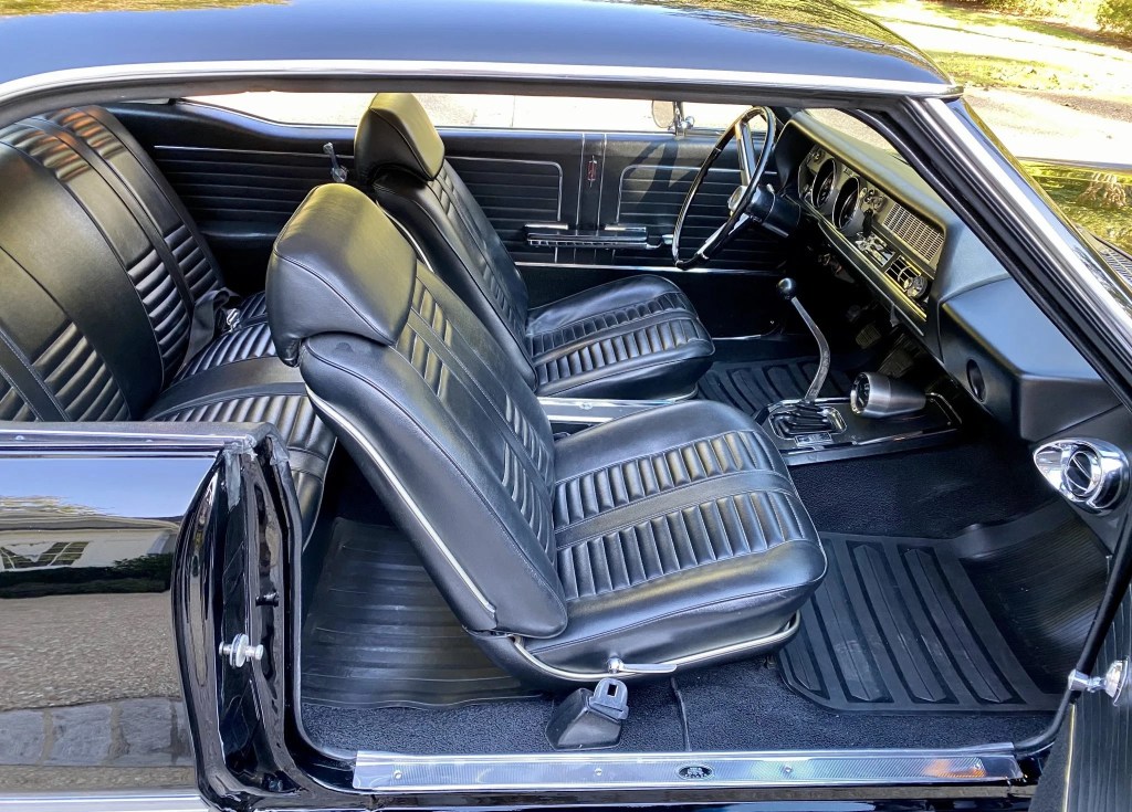 The black-vinyl interior of a black 1966 Oldsmobile 442 with a Hurst shifter