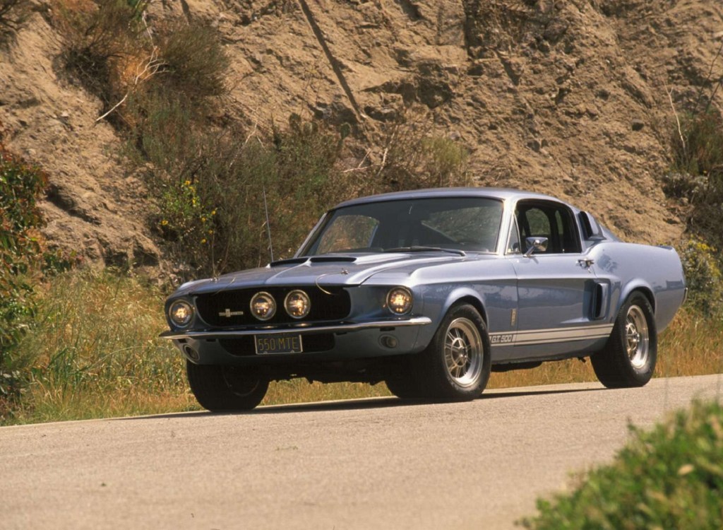 A blue-and-white 1967 Shelby GT500 Mustang driving down a canyon road