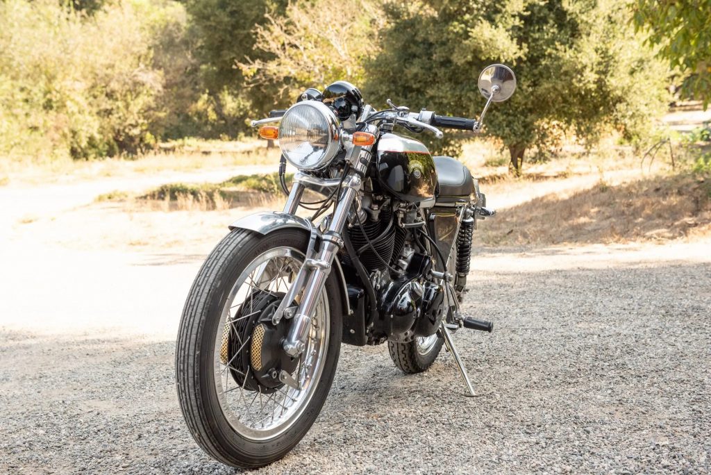 The front 3/4 view of a black-and-silver 1968 Egli-Vincent by Godet on a sunlit gravel driveway