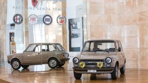 A brown 58-hp 1971 Autobianchi A112 Abarth in front on a mirrored Stellantis stand