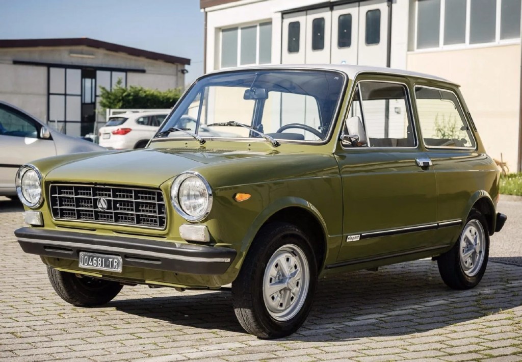 A green 1974 Autobianchi A112 parked in a crowded parking lot