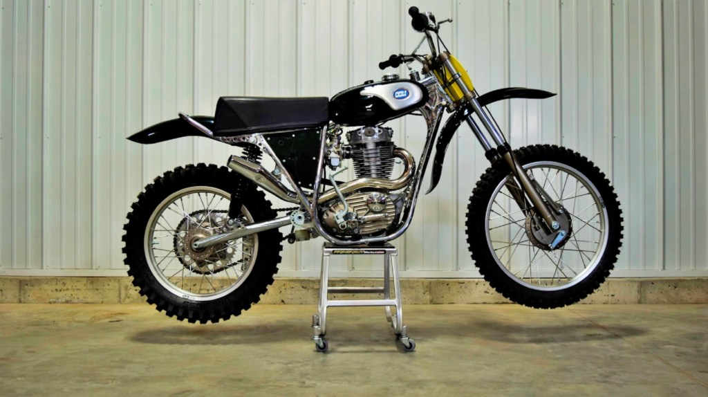 A black-and-chrome 1974 CCM 605 John Banks Replica motocross motorcycle on its stand in a warehouse