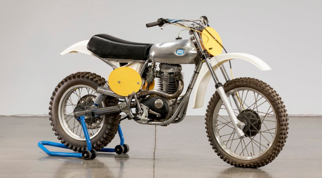 A yellow-white-and-chrome 1976 CCM Cross 4-Stroke motorcycle on a blue rear-wheel stand