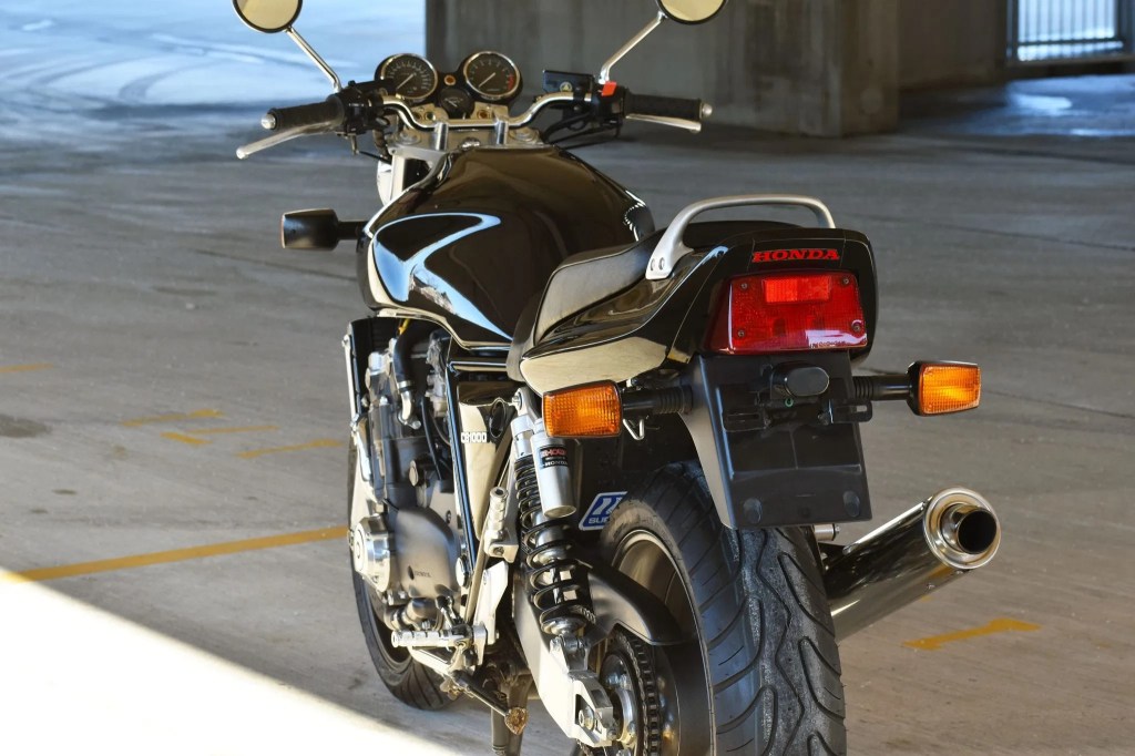 The rear 3/4 view of a black 1994 Honda CB1000 Super Four in a sunny parking garage
