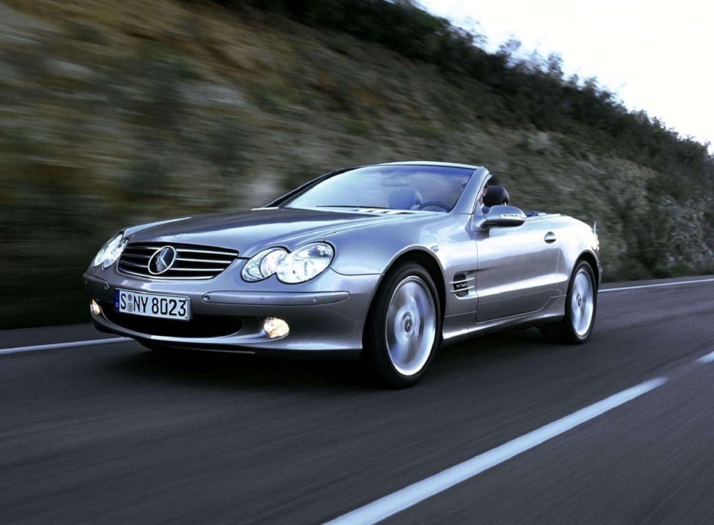 A silver 2004 Mercedes-Benz SL600 with its roof down driving down the road by a rocky cliff