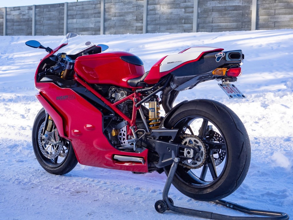 The rear 3/4 view of a red-and-white 2005 Ducati 999R on a rear-wheel stand parked on snow