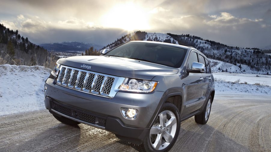 A grey 2011 Jeep Grand Cherokee driving down a road with a setting sun in the background