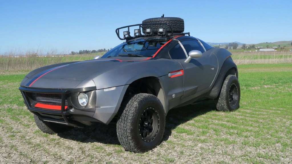 A gray-and-red 2011 Local Motors Rally Fighter with a roof-mounted basket in a field