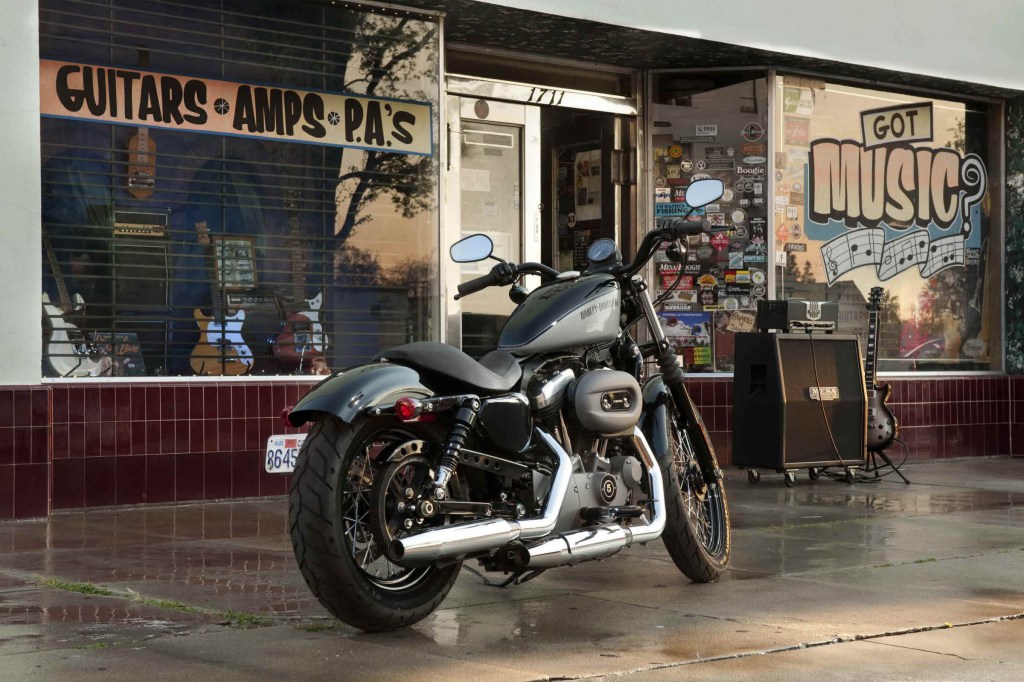 The rear 3/4 view of a gray-and-black 2012 Harley-Davidson Nightster parked by a record store