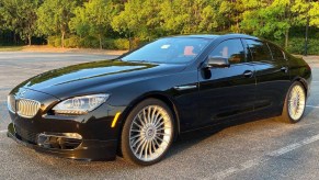 A black 2015 BMW Alpina B6 xDrive Gran Coupe parked on a sunset-lit tree-lined parking lot