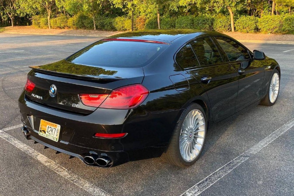 The rear 3/4 view of a black 2015 BMW Alpina B6 xDrive Gran Coupe parked on a sunset-lit tree-lined parking lot