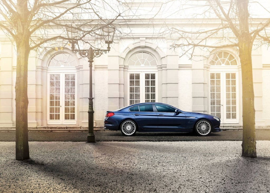 The side view of a dark-blue 2015 BMW Alpina B6 xDrive Gran Coupe by a white old building