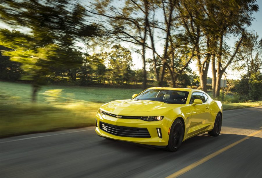 A yellow 2017 Chevy Camaro driving down a country road with trees in the background