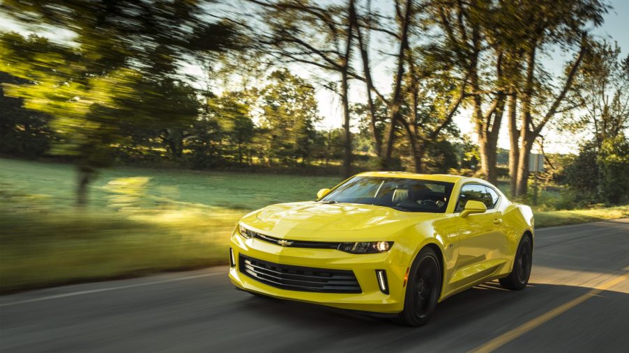 A yellow 2017 Chevy Camaro driving down a country road with trees in the background