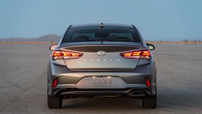 A rear view of a dark-gray metallic 2019 Hyundai Sonata midsize sedan parked on a large expanse of asphalt in a desert