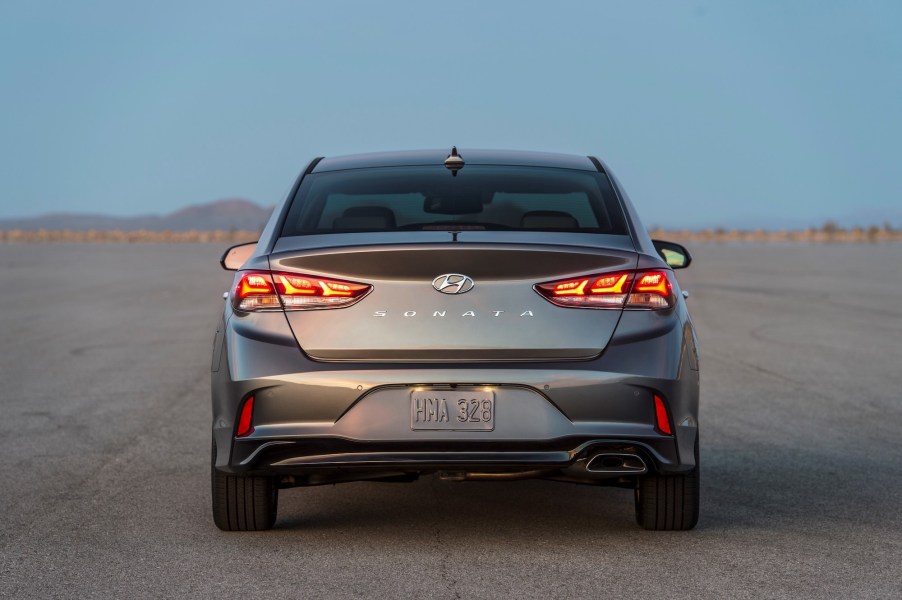 A rear view of a dark-gray metallic 2019 Hyundai Sonata midsize sedan parked on a large expanse of asphalt in a desert