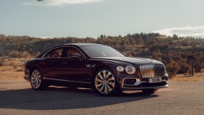 A maroon 2020 Bentley Flying Spur parked by sunlit tree-covered hills