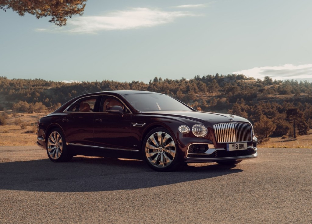 A maroon 2020 Bentley Flying Spur parked by sunlit tree-covered hills