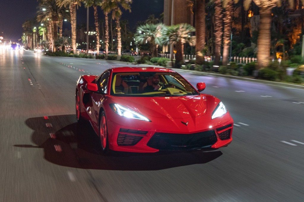 A red 2020 Chevy Corvette Stingray sports car travels at night on a multilane highway with palm trees in the median
