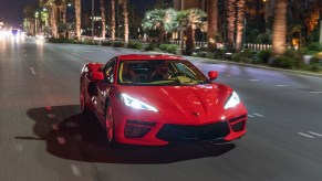 A red 2020 Chevy Corvette Stingray sports car travels at night on a multilane highway with palm trees in the median