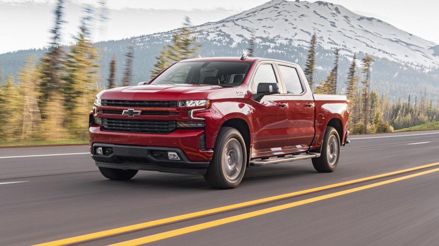 A red 2020 Chevrolet Silverado Diesel full-size pickup truck travels on a four-lane highway past pine trees and a snow-capped mountain