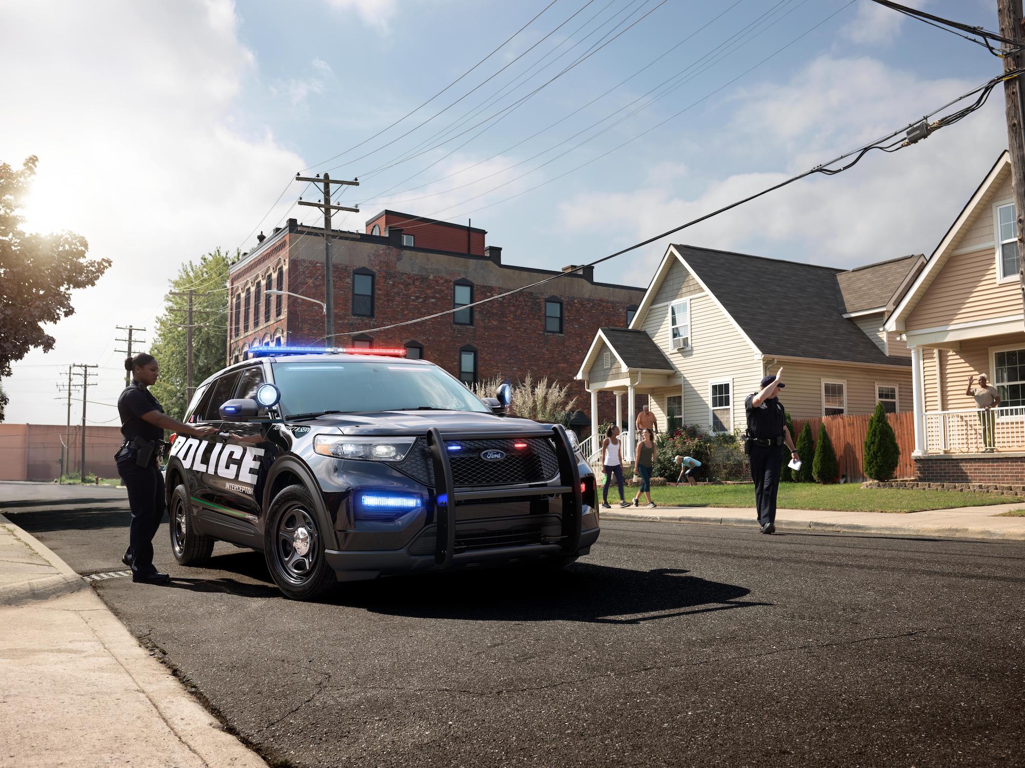 A 2020 Ford Police Interceptor Utility Hybrid SUV parked on a residential street with two police officers standing nearby