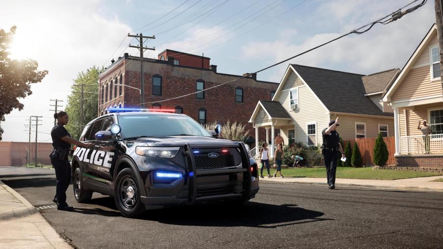 A 2020 Ford Police Interceptor Utility Hybrid SUV parked on a residential street with two police officers standing nearby
