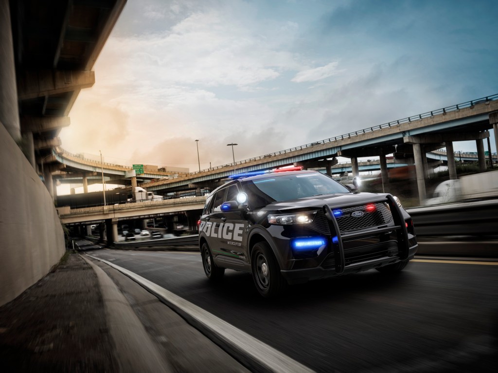 A black 2020 Police Interceptor Utility vehicle with its lights on travels on a highway entrance ramp
