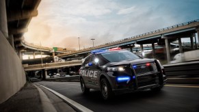 A black 2020 Police Interceptor Utility vehicle with its lights on travels on a highway entrance ramp
