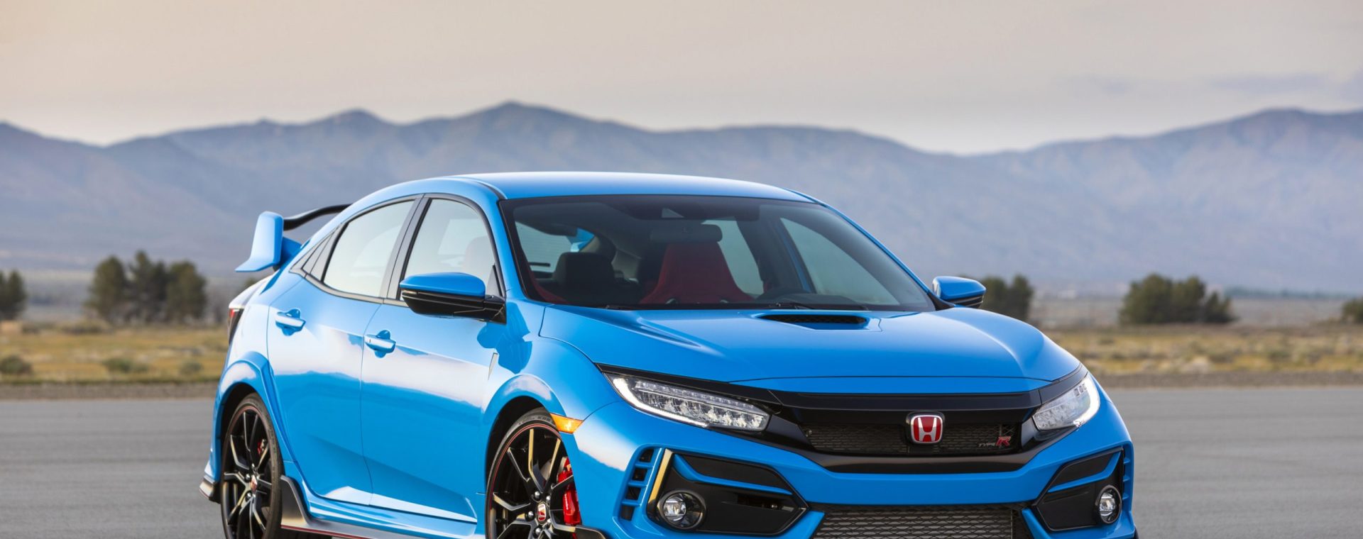 A blue 2020 Honda Civic Type R parked on display with a mountain range in the background