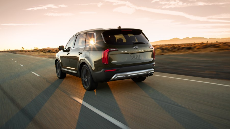 A side-rear view of a dark-colored 2020 Kia Telluride midsize SUV driving into the sunset