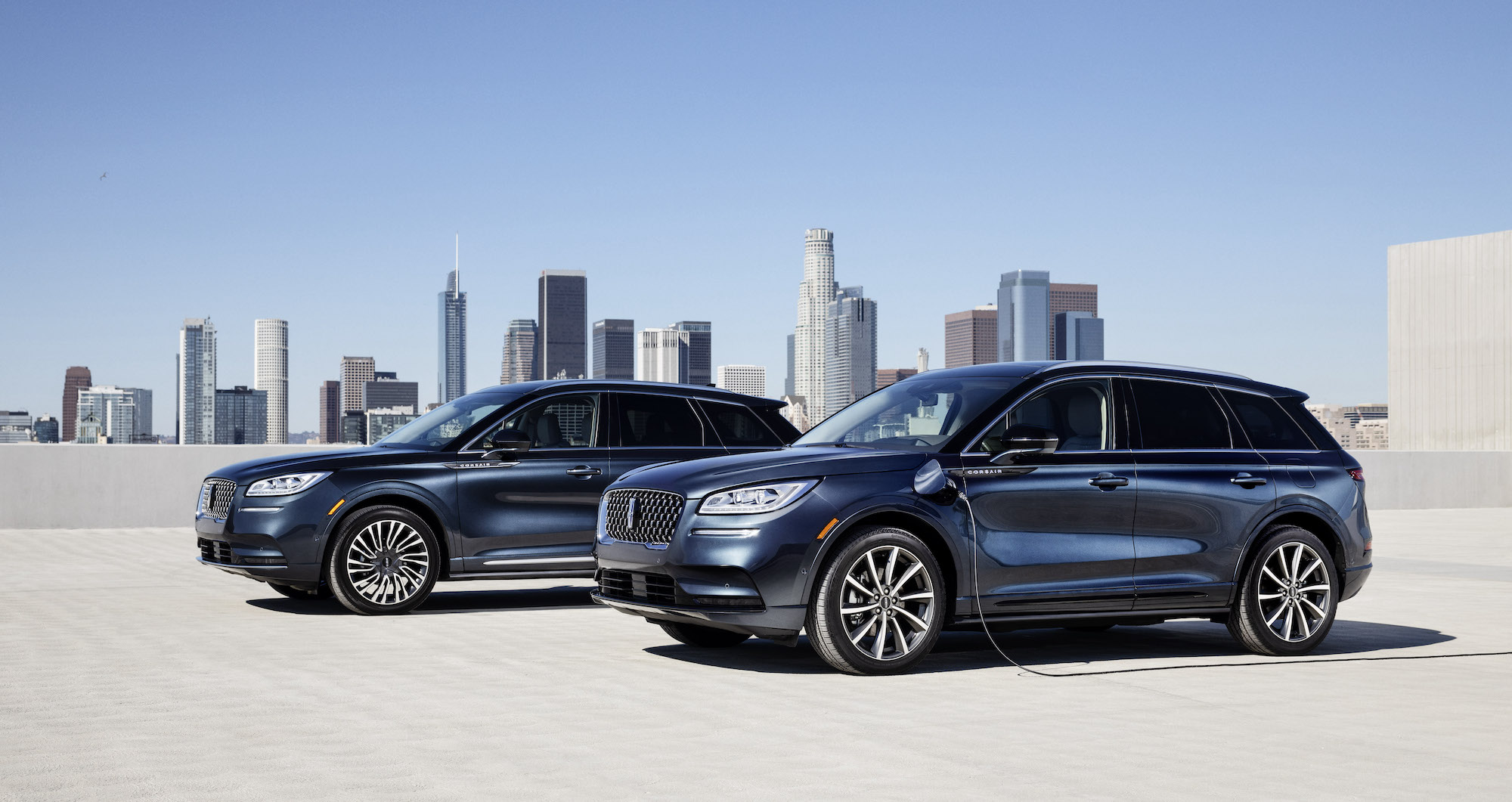 Two dark-blue 2020 Lincoln Corsair luxury compact crossover SUVs parked on a building's roof with a city skyline in the background