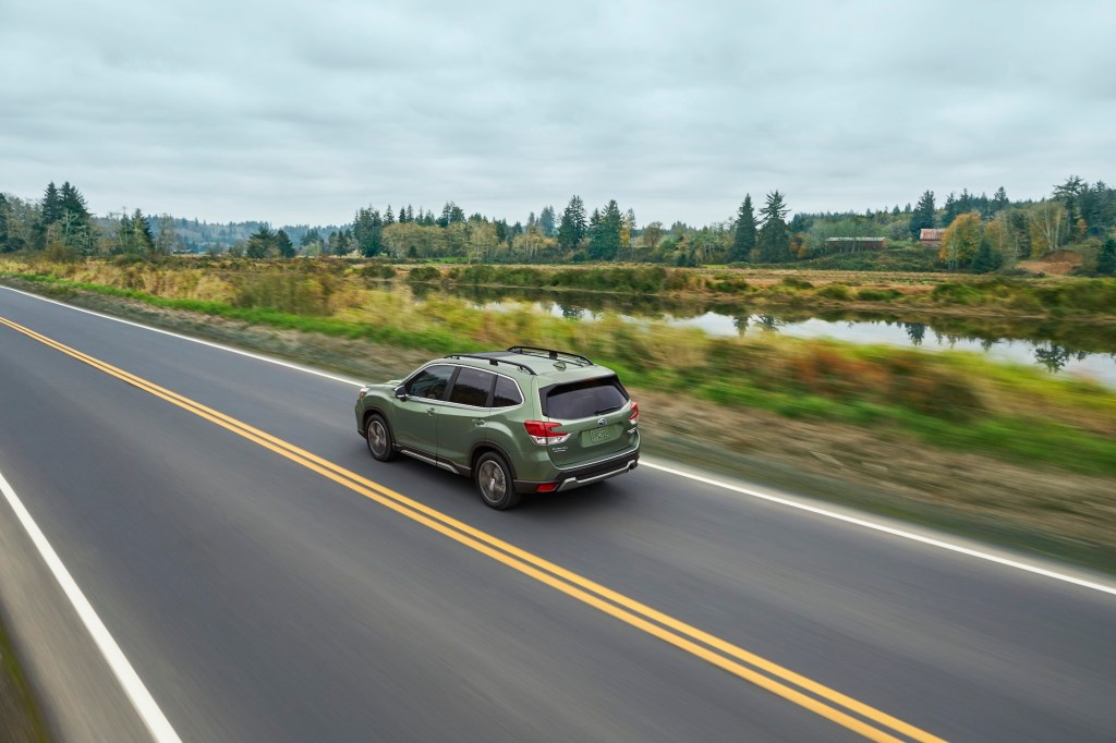 A green 2020 Subaru Forester compact crossover SUV travels on a two-lane highway past foliage and a canal