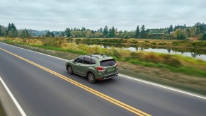 A green 2020 Subaru Forester compact crossover SUV travels on a two-lane highway past foliage and a canal
