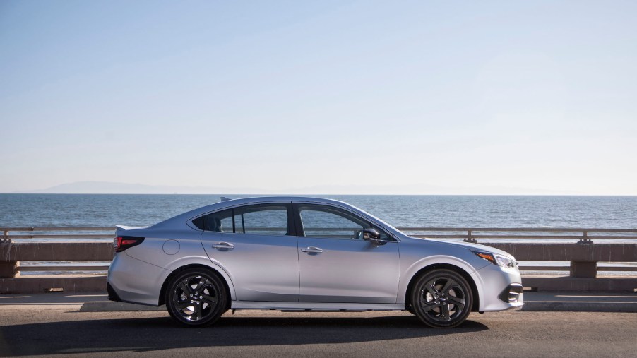 A silver 2020 Subaru Legacy Sport midsize sedan parked on the pavement in front of a large body of water on a cloudless day