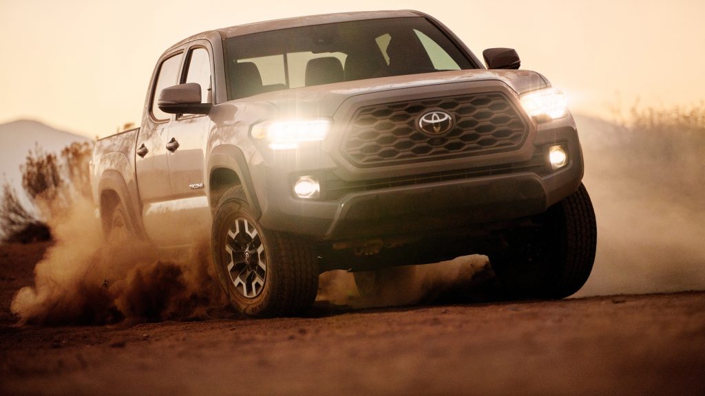 A white 2020 Toyota Tacoma TRD Off Road driving at sunrise kicking up sand and showing off