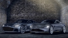 A gray 2021 Aston Martin Vantage 007 Edition and DBS Superleggera 007 Edition by a cobblestone wall