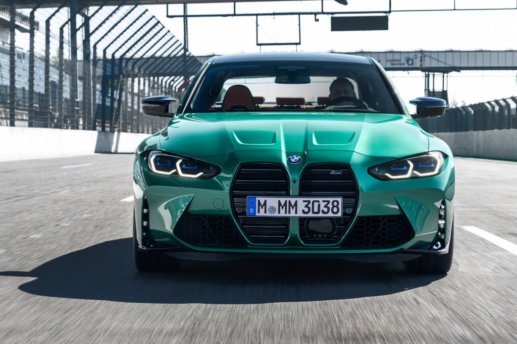 Front view of a green 2021 BMW M3 sports sedan traveling on a racetrack's straightaway
