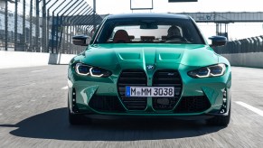 Front view of a green 2021 BMW M3 sports sedan traveling on a racetrack's straightaway