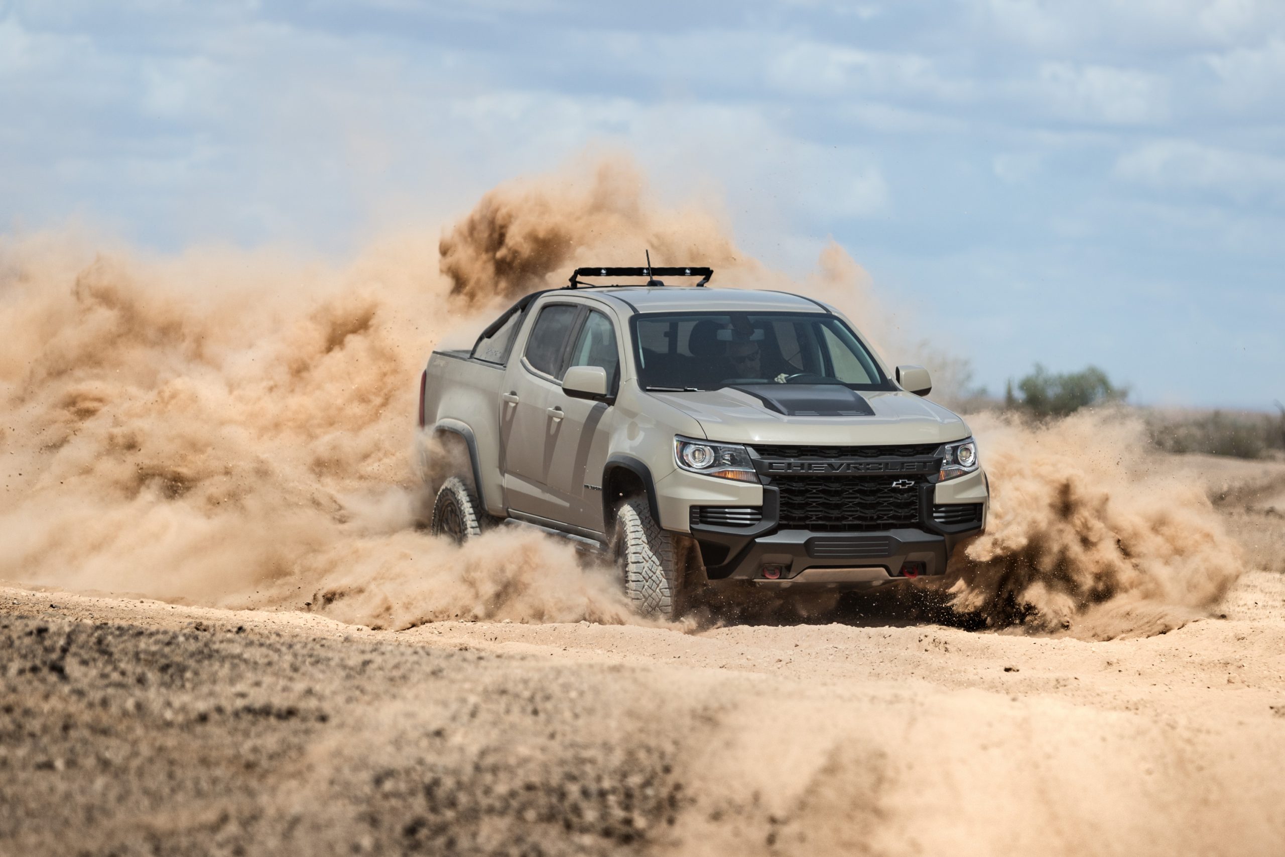 A grey and black 2021 Chevy Colorado ZR2 turbo-diesel pickup truck driving off-road, kicking up sand